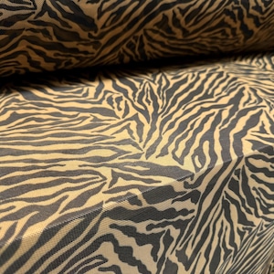 May include: A close-up of a brown and black tiger stripe patterned fabric. The fabric is sheer and has a mesh-like texture.