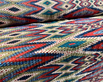 May include: Close-up of a fabric with a colorful geometric pattern. The pattern features red, blue, green, and white colors in a repeating diamond and chevron design.