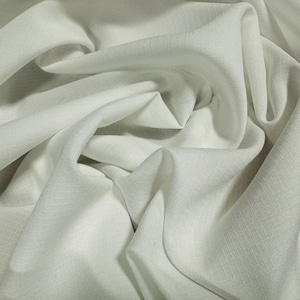 Può includere: Un primo piano di un tessuto di lino bianco con una texture sottile. Il tessuto è piegato e drappeggiato, mostrando la sua qualità morbida e fluida.