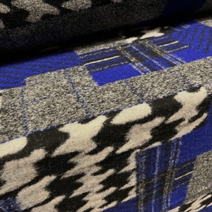 Pode incluir: Um close-up de um tecido com um design de patchwork. O tecido é feito de um material macio e felpudo e apresenta uma combinação de cores preto, branco, cinza e azul. O tecido é disposto em um padrão geométrico, com quadrados e retângulos de diferentes tamanhos e cores.