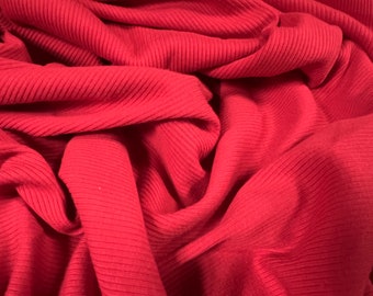 May include: Red ribbed fabric with a soft, textured surface. The fabric is folded and draped, showing the texture and color.