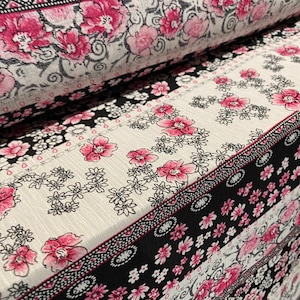 May include: A close-up of a fabric with a black and white floral pattern. The fabric has a pink and white stripe pattern along the bottom edge.