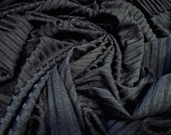 May include: Close-up of a dark gray ribbed fabric with a textured surface. The fabric is folded and draped, creating a soft and flowing look.