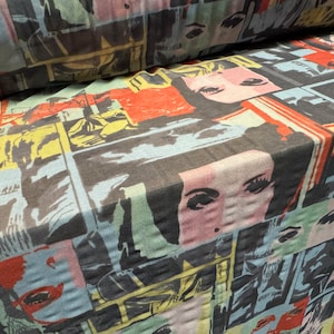 May include: A black fabric with a colourful print of repeated images of faces. The faces are in a comic book style with bold lines and bright colours.