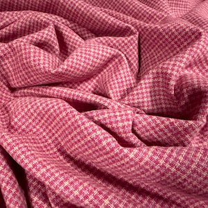 Op de afbeelding: Close-up van een textiel met een klein ruitpatroon in roze en witte tinten. De stof is gedrapeerd, waardoor plooien en schaduwen ontstaan die de textuur en kleurvariaties benadrukken. Ideaal voor naai- en knutselprojecten.