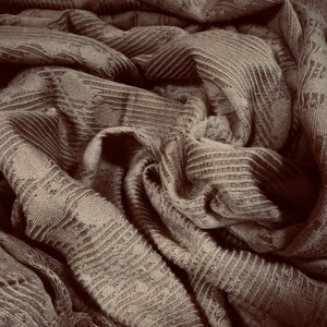 May include: Close-up of a brown fabric with a textured, ribbed pattern. The fabric is folded and draped, creating a soft and cozy look.