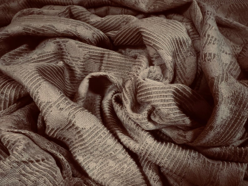 May include: Close-up of a brown fabric with a textured, ribbed pattern. The fabric is folded and draped, creating a soft and cozy look.