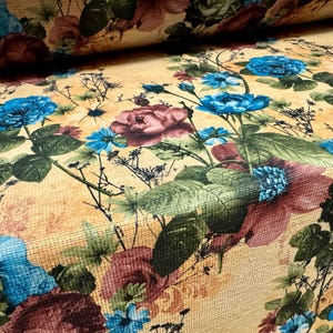 May include: Floral fabric with a repeating pattern of blue and burgundy roses, green leaves, and small white flowers on a tan background. The fabric has a textured appearance, suggesting a woven material. The design is reminiscent of vintage floral prints.