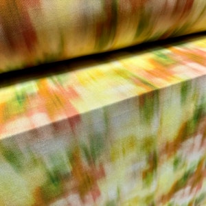 May include: Close-up of a yellow fabric with a blurred abstract pattern in shades of orange, green, and white.