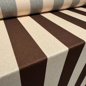 May include: Close-up of a fabric roll featuring a bold striped design. Wide, alternating stripes of brown and beige create a striking visual effect. The fabric has a textured surface, suggesting a durable material suitable for upholstery or home decor projects.