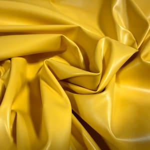 May include: Close-up of a sheet of bright yellow fabric with a glossy finish. The material is heavily creased, creating shadows and highlights that emphasize its texture. The fabric appears to be a synthetic material, possibly vinyl or faux leather.