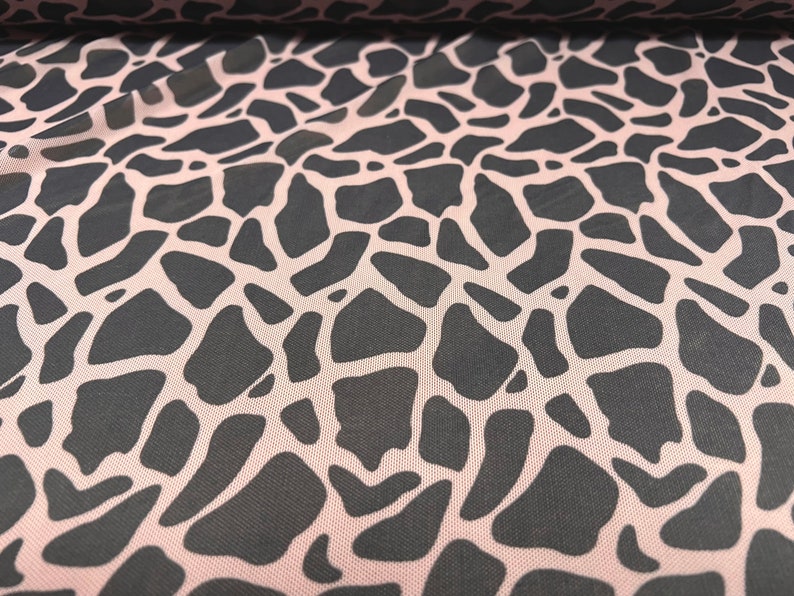 May include: Pink mesh fabric with a black giraffe print pattern.