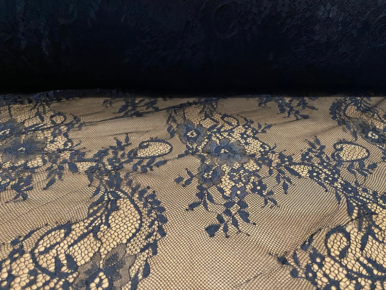 May include: Black lace fabric with a delicate floral pattern. The lace is sheer and has a soft, flowing texture.