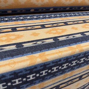 Puede incluir: Un rollo de tela tejida con un patrón repetitivo de rayas horizontales en tonos azul marino, azul claro y crema. El diseño incluye formas geométricas y motivos de diamantes intercalados entre las líneas azules sólidas y discontinuas.
