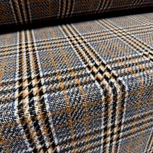 May include: A woven fabric featuring a classic plaid pattern in shades of blue, grey, black, and tan. The textile displays a textured, multi-coloured grid design with intersecting lines of varying thickness, creating a structured and repeating geometric motif.