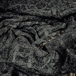 Pu&ograve; includere: Tessuto di pizzo nero con un motivo delicato. Il tessuto &egrave; drappeggiato e piegato, creando un design testurizzato e intricato.