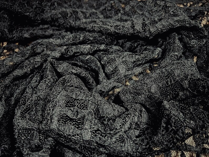 Pu&ograve; includere: Tessuto di pizzo nero con un motivo delicato. Il tessuto &egrave; drappeggiato e piegato, creando un design testurizzato e intricato.