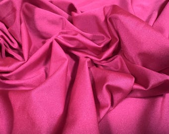 May include: A close-up of a bright pink fabric with a smooth, shiny texture. The fabric is folded and draped, showing its flexibility and drape.