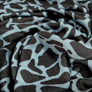 May include: Close-up of a blue and black fabric with a textured, abstract pattern. The fabric is wrinkled and folded, showing the texture of the material.