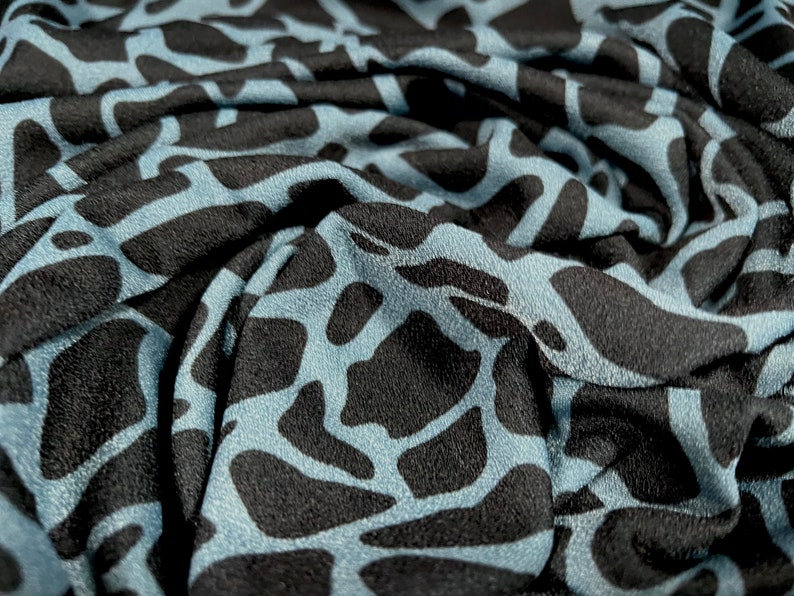 May include: Close-up of a blue and black fabric with a textured, abstract pattern. The fabric is wrinkled and folded, showing the texture of the material.