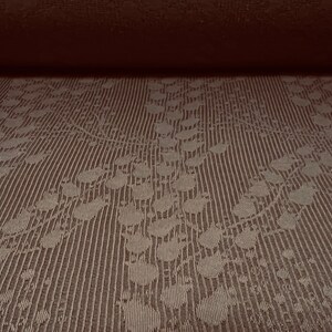 May include: Close-up of a brown fabric with a subtle embossed pattern of leaves and dots. The fabric has a textured, woven look.