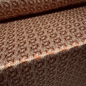 May include: Brown fabric with a white patterned design. The pattern is a repeating geometric design with a floral motif.