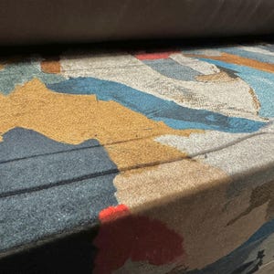 Puede incluir: Primer plano de una tela con un patrón abstracto colorido. La tela presenta tonos de azul, marrón, rojo y blanco. La tela tiene una superficie texturizada.