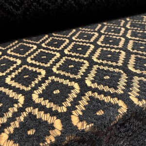 Op de afbeelding: Zwarte stof met een geometrisch patroon van beige vierkanten. De stof heeft een textuur en is geweven.