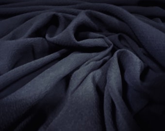 May include: A close-up of a dark blue fabric with a textured surface. The fabric is folded and draped, creating soft folds and wrinkles.