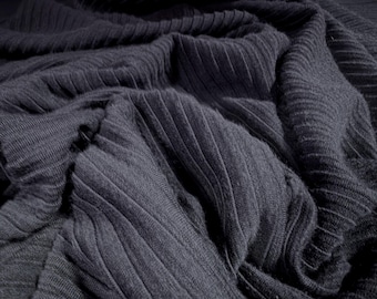 May include: Close-up of a dark gray, ribbed knit fabric. The fabric is heavily textured with vertical ridges and folds, creating shadows and depth. The material appears soft and pliable, with a subtle sheen.