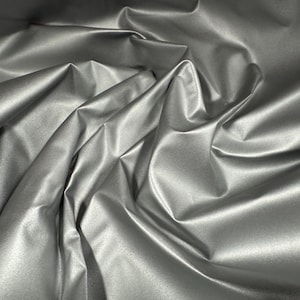 May include: Silver metallic fabric with a smooth, shiny finish. The fabric is draped and folded, showcasing its texture and drape.