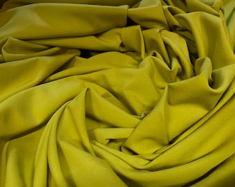 May include: A close-up of a soft, green fabric with a smooth texture. The fabric is folded and draped, creating a sense of movement and flow.