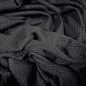May include: Close-up of a black waffle knit fabric with a textured surface. The fabric is folded and draped, creating a soft and cosy look.