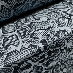 May include: Close-up of a fabric with a black and white snake skin pattern. The fabric has a light blue background.