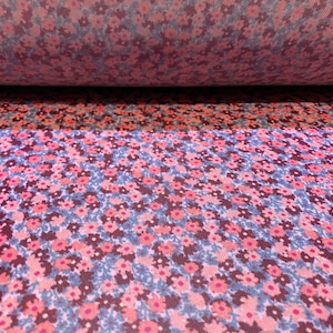 May include: Close-up of a pink and blue floral fabric with a small, repeating pattern of flowers. The fabric is rolled up, showing the pattern from two different angles.