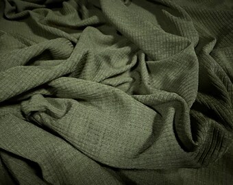 May include: Close-up of olive green ribbed knit fabric. The fabric is draped and folded, creating shadows and texture. The knit pattern is visible, adding to the fabric's visual interest. Ideal for apparel or home decor projects.