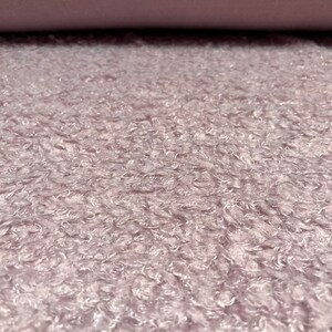 Pu&ograve; includere: Primo piano di un tessuto morbido, di colore lilla chiaro, con una texture soffice. Il tessuto ha un leggero effetto iridescente.