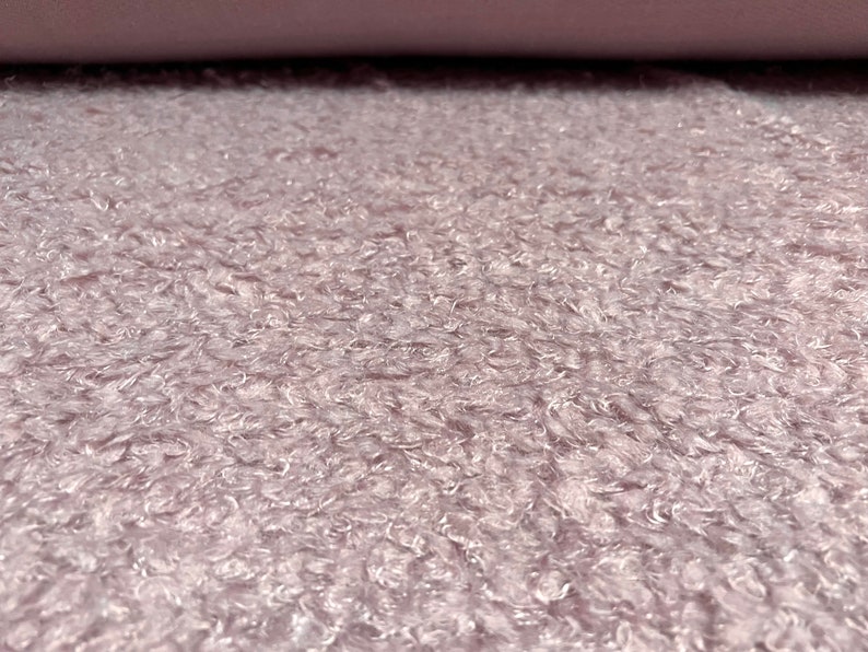 Pu&ograve; includere: Primo piano di un tessuto morbido, di colore lilla chiaro, con una texture soffice. Il tessuto ha un leggero effetto iridescente.