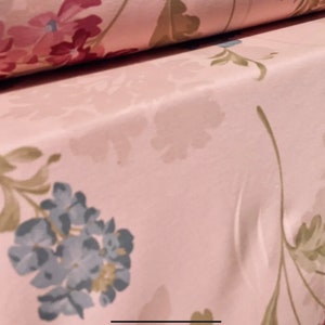 May include: Pink fabric with a floral pattern. The fabric features a light pink background with a repeating pattern of blue and green flowers and leaves.