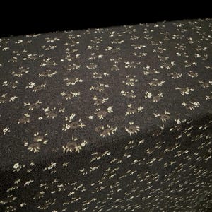 May include: A black fabric featuring a repeating pattern of small, white floral clusters. The material has a textured surface and is draped to show the fabric's fold and depth, highlighting the consistent distribution of the tiny white flower print.