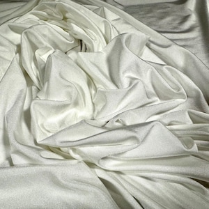 May include: White fabric with a smooth, silky texture. The fabric is draped and folded, creating soft, flowing curves.