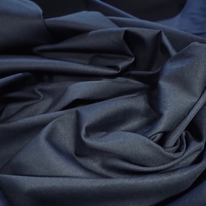 May include: Close-up of a dark blue fabric with a smooth, slightly textured surface. The fabric is folded and draped, creating soft, flowing lines.