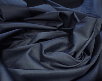 May include: Close-up of a dark blue fabric with a smooth, slightly textured surface. The fabric is folded and draped, creating soft, flowing lines.
