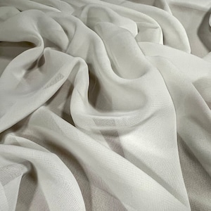 May include: White sheer fabric with a smooth, silky texture. The fabric is draped and folded, creating soft, flowing lines.
