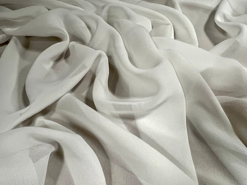 May include: White sheer fabric with a smooth, silky texture. The fabric is draped and folded, creating soft, flowing lines.