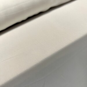May include: Close-up of a white fabric with a smooth, slightly textured surface. The fabric is folded over itself, creating a diagonal line.