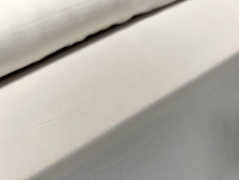 May include: Close-up of a white fabric with a smooth, slightly textured surface. The fabric is folded over itself, creating a diagonal line.