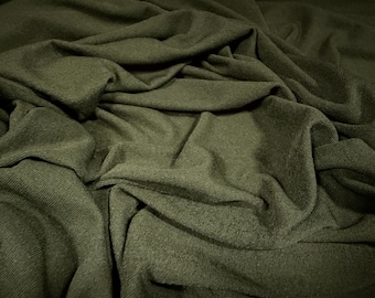 May include: Close-up of olive green fabric with a textured knit appearance. The fabric is draped and folded, creating shadows and highlights that emphasize its texture and depth. The material appears soft and pliable.