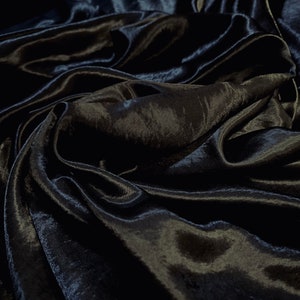 May include: Close-up of a black satin fabric with a smooth, silky texture. The fabric is draped and folded, creating soft, flowing lines.