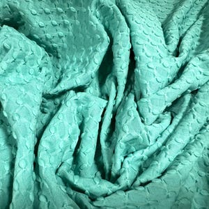May include: A close-up of a teal textured fabric with a raised pattern of small circles. The fabric is soft and has a slightly bumpy texture.